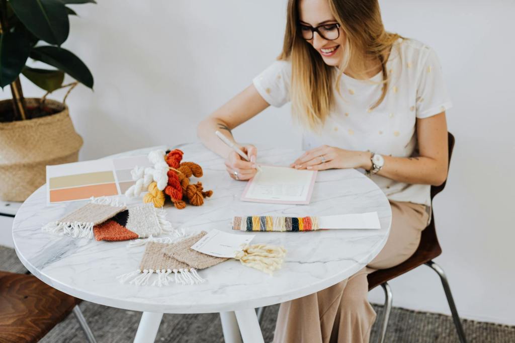 woman with yarn samples writing notes in a pad
